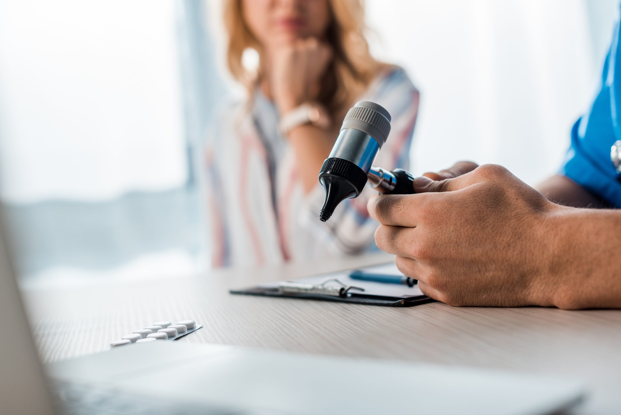 Audiologist using an otoscope to examine a patient's ear during a hearing checkup, discussing potential need for hearing aids.